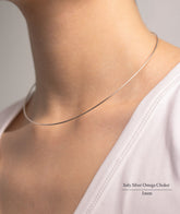 Fine jewellery, silver jewellery, tarnish-free, hypoallergenic, Side view of Silver Omega choker necklace with a diameter of 1mm on a person wearing a white top against a neutral background